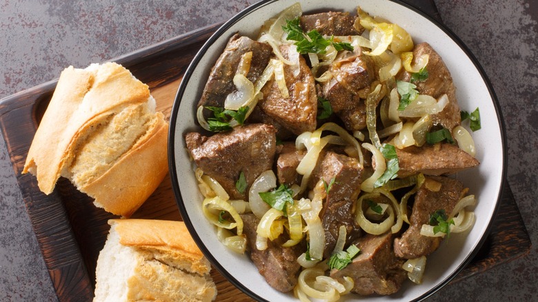 fried beef liver and onions in bowl with bread on the side
