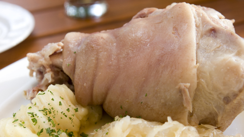 A close-up shot of eisbein served with potatoes and sauerkraut on a plate