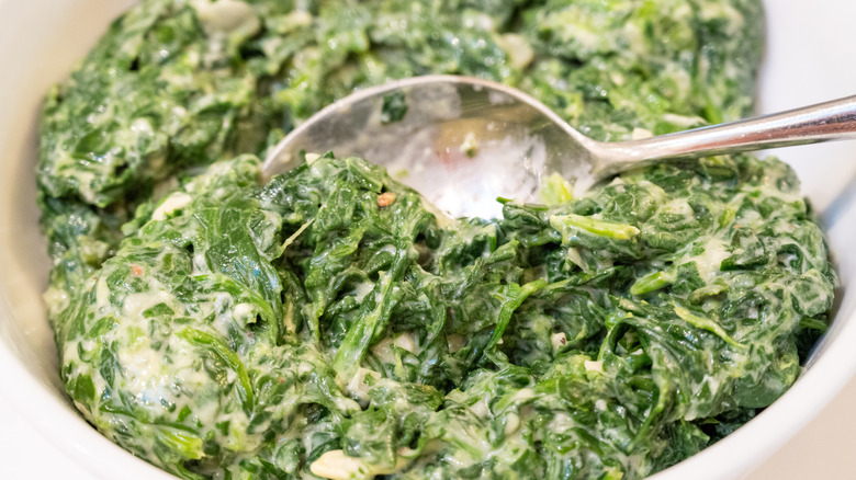 A bowl of creamed spinach with a spoon in it