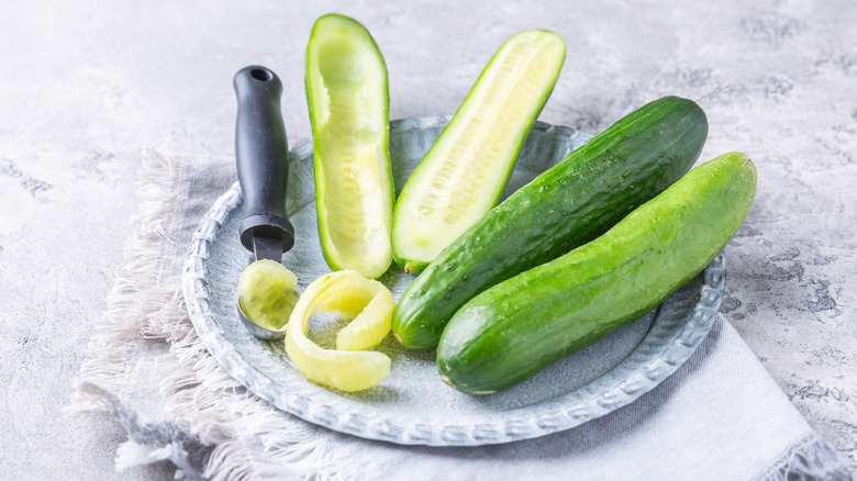 A plate of cucumbers next to a scooper and some cucumber flesh that's been removed