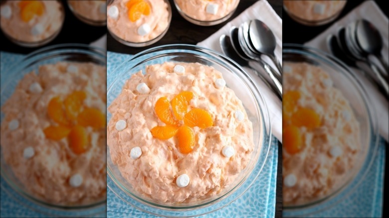 A bowl of orange fluff salad next to a pile of spoons