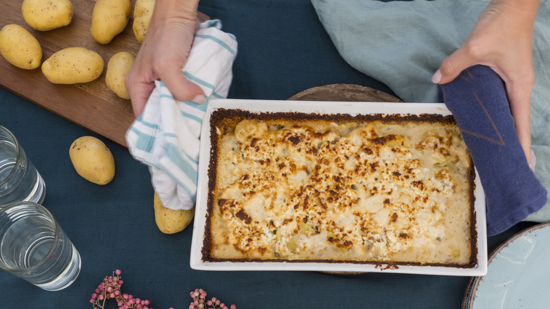 A baked casserole next to a cutting board of raw potatoes