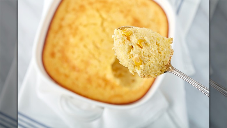 A pan of scalloped corn with a spoon scooping some out
