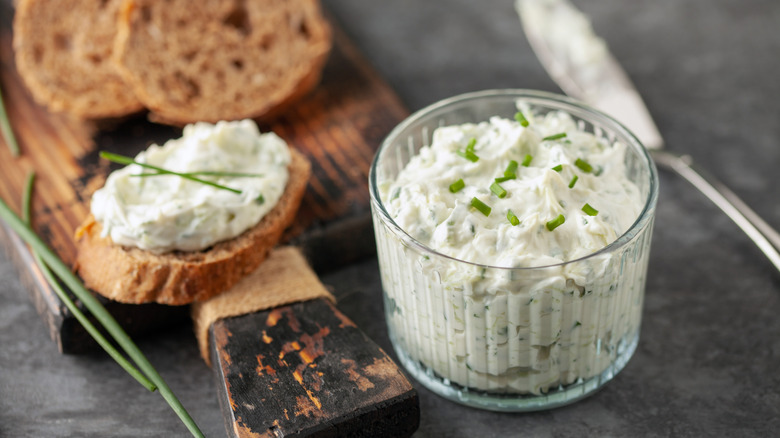 Benedictine spread in glass cup next to bread on cutting board