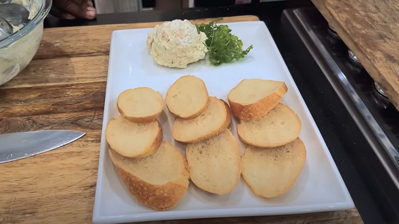 Scoop of shrimp butter next to parsley on white platter with bread slices