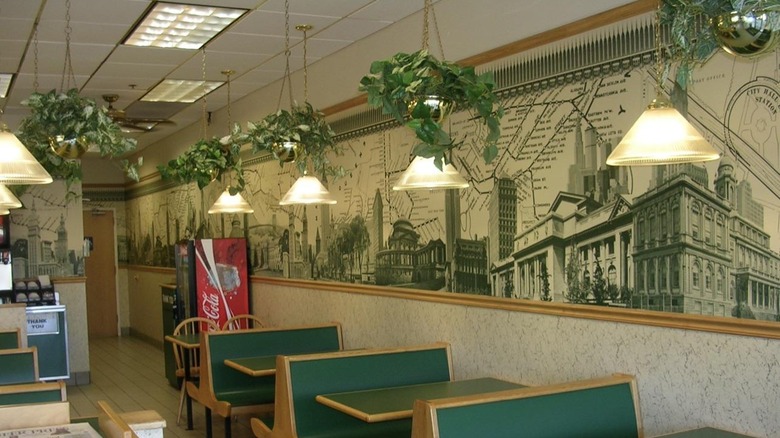 Interior of an old-school Subway restaurant with green booths and subway-themed wallpaper