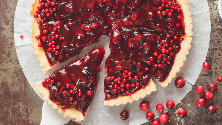 Sliced cranberry pie with one slice being removed and loose cranberries