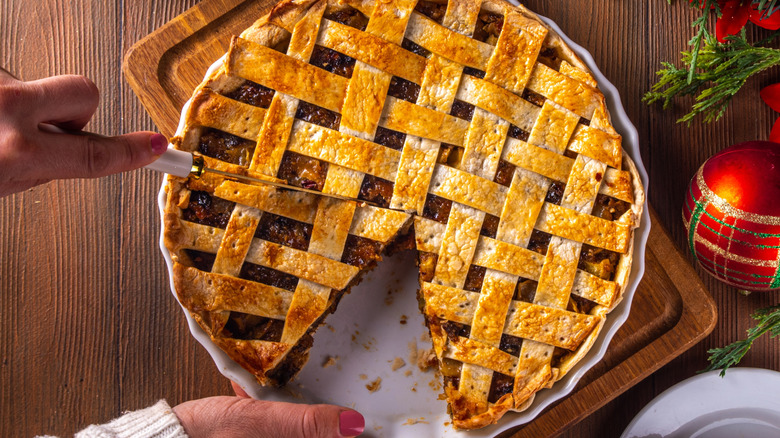 Hands cutting slices from a mincemeat pie