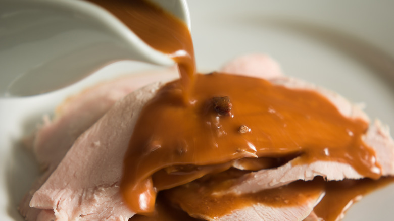 A gravy boat pours giblet gravy on slices of turkey.