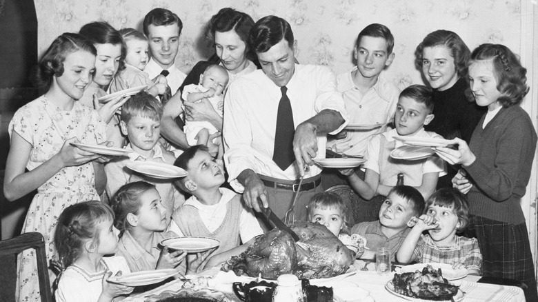 Vintage black-and-white photo of a man carving a turkey for a large family..