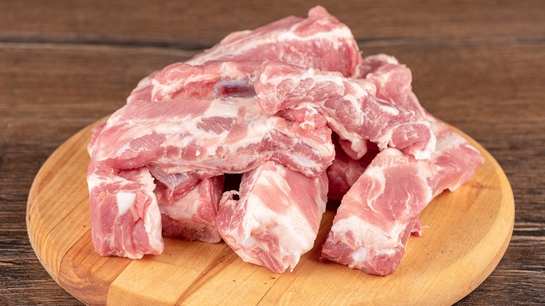 A pile of raw cut pork ribs on a wooden cutting board.