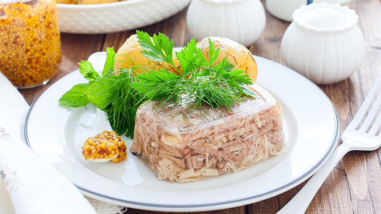 Turkey aspic on a white plate with boiled potatoes and a dollop of mustard.
