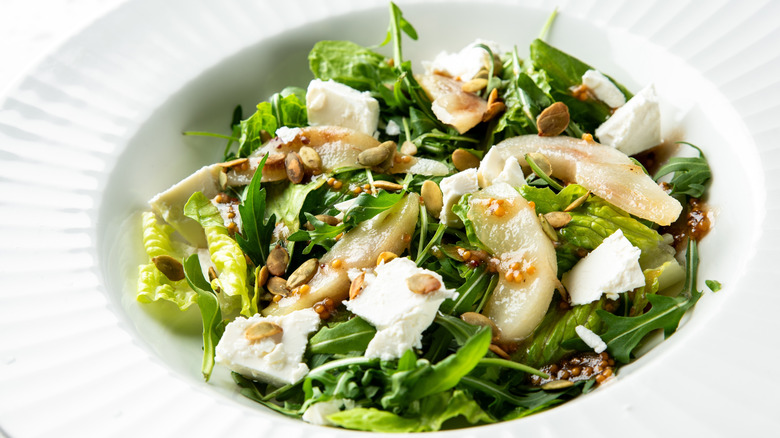 A salad made with arugula, sliced pears, pumpkin seeds, and feta cheese