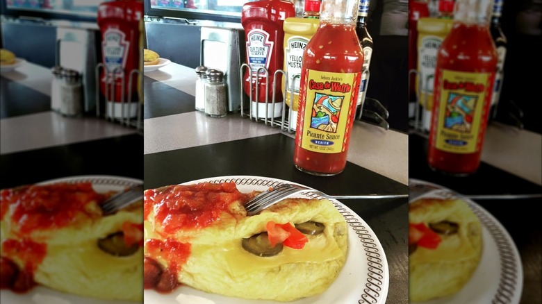 An omelet topped with Casa de Waffle picante sauce in front of the glass jar of sauce