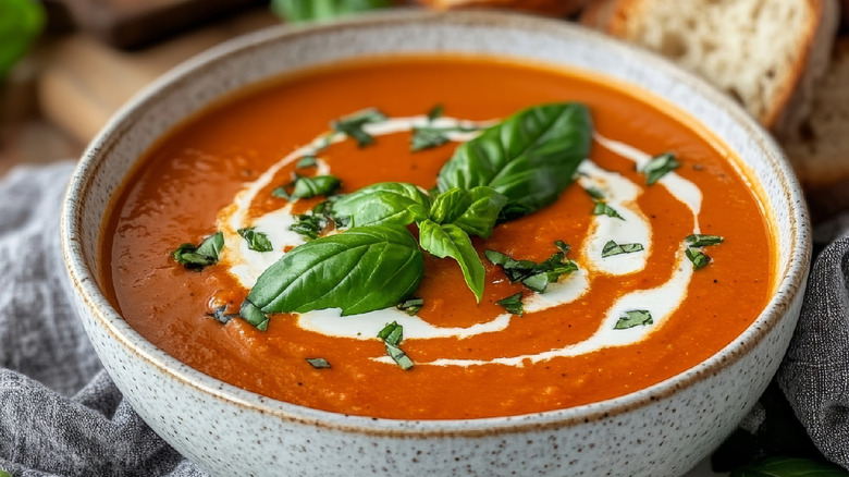 A bowl of cream of tomato soup with a swirl of cream topped with basil leaves