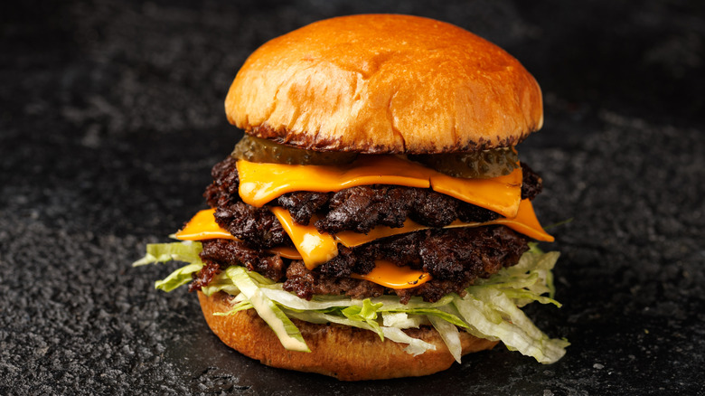 A smash burger with three patties, lettuce, cheese, and pickles on a toasted bun
