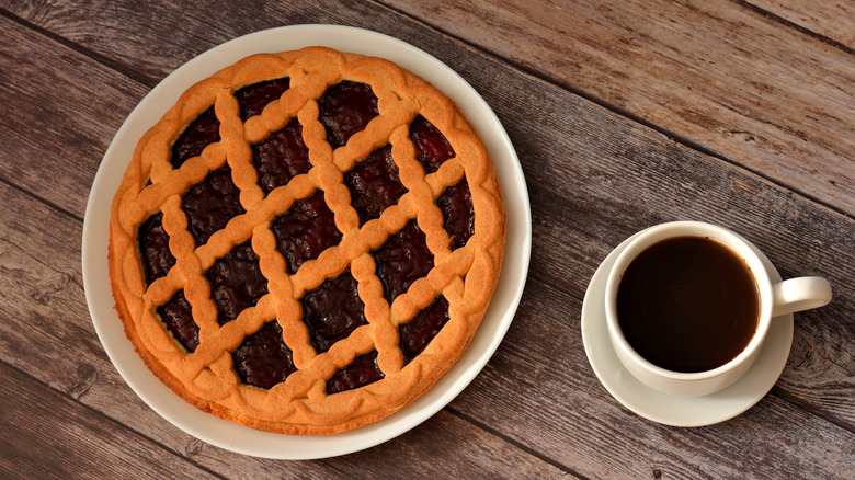 A whole cherry pie next to a mug of coffee