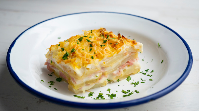 A square of potato lasagna plated with bechamel sauce and chopped parsley