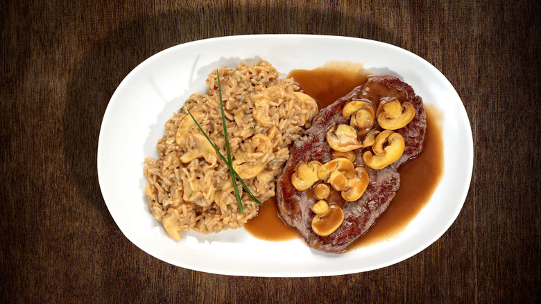 Steak Diane with mushroom risotto and sauce on a white plate