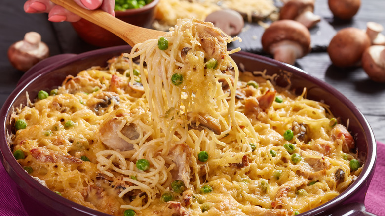 A wooden spoon scooping turkey Tetrazzini out of a pot, ingredients in the background