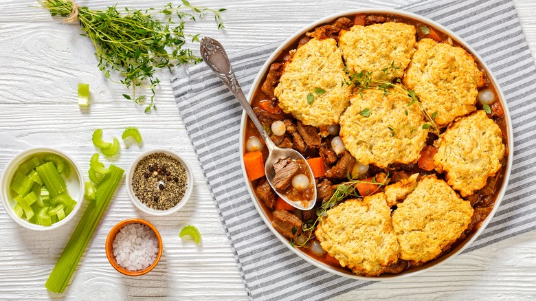A bowl of winter vegetable cobbler with beef next to sliced celery and herbs and spices