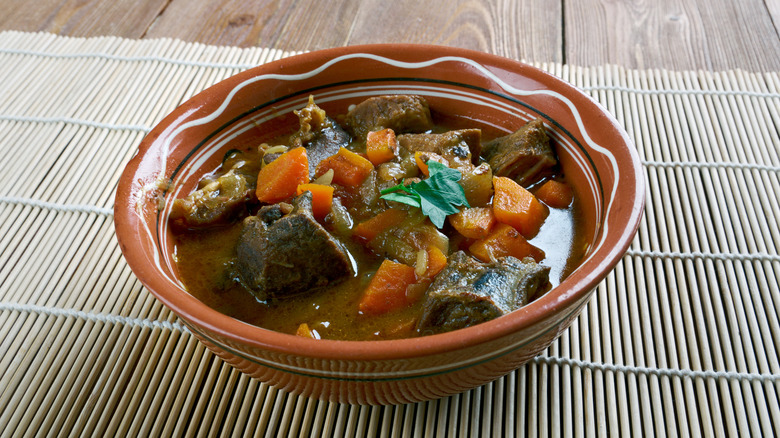 Terra cotta bowl of brothy soup with meat chunks, carrots