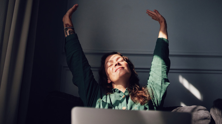 woman sitting behind laptop raising hands in happiness