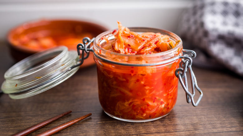 A glass jar of kimchi on a wooden surface