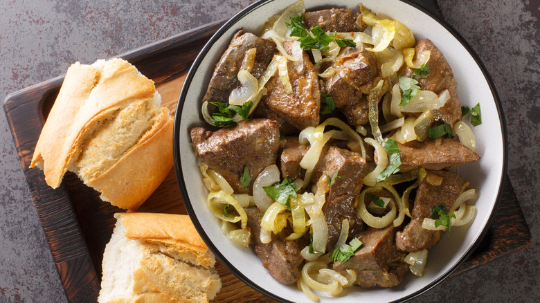 Fried liver and onions on board with baguette pieces