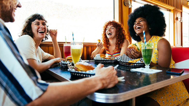 Happy friends eating at an '80s-style diner together.