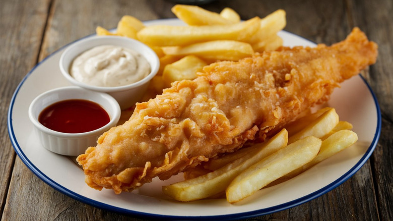Fish and chips on white plate with two cups of sauce