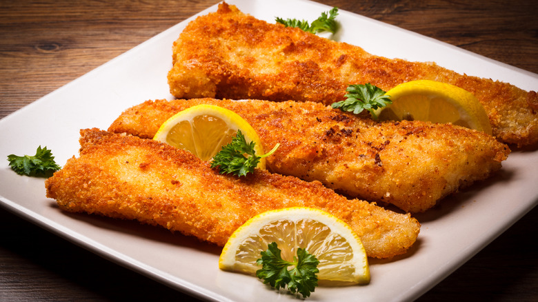 Fried fish with lemon wedges on garnish atop white plate and wooden table
