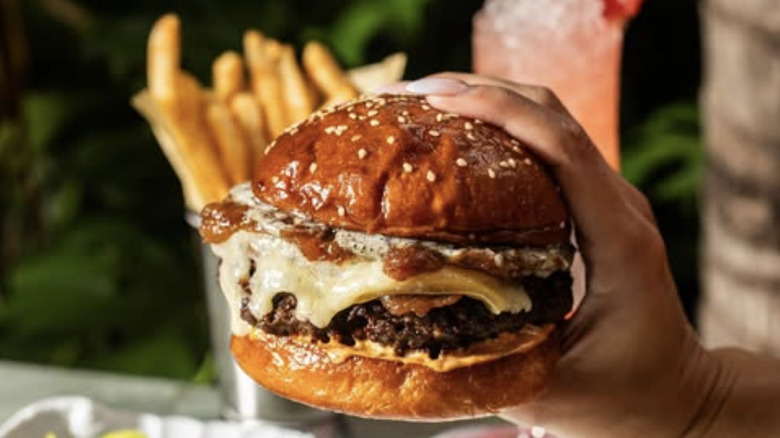 Sunny's burger held up in front of fries and pink drink
