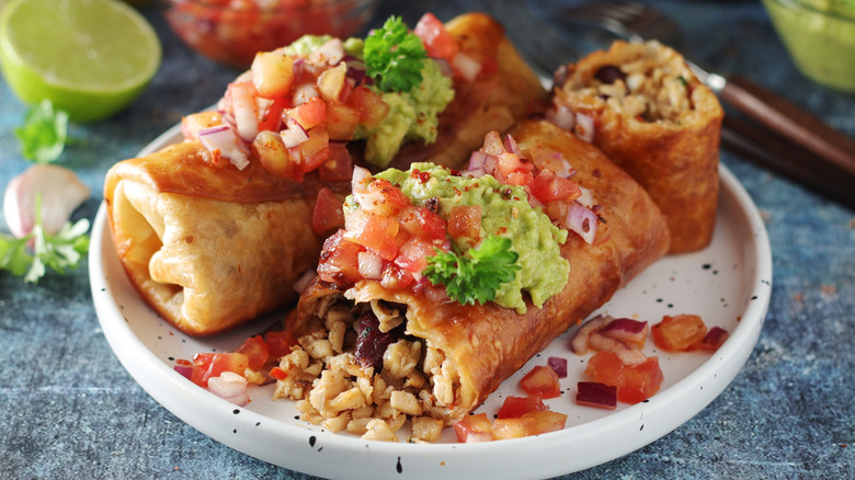 Chimichanga with tomatoes and guacamole on white plate