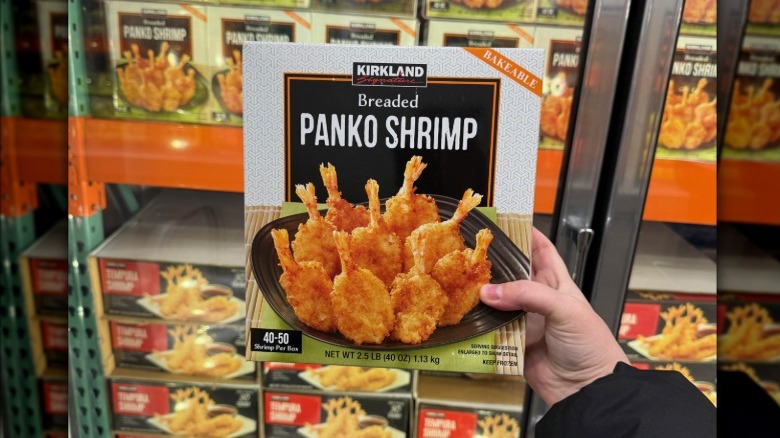 Hand holding a box of Kirkland Signature breaded panko shrimp in front of a freezer