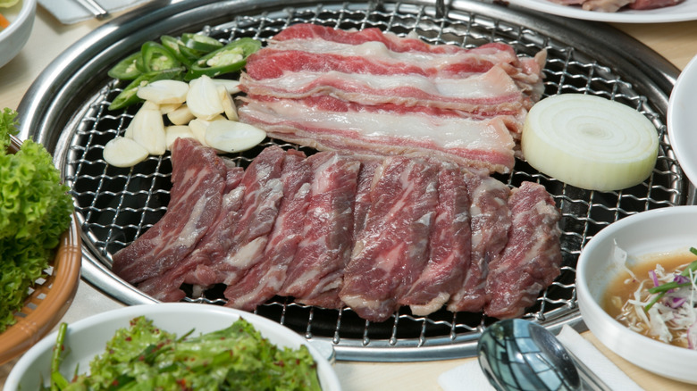 Cuts of pork and beef with a thick onion slice cooking on the grill at a Korean barbecue