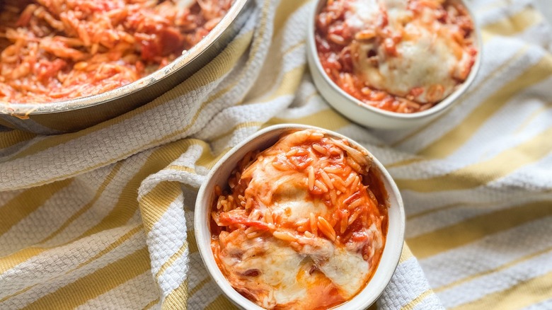 Two bowls and pot of cheesy orzo and tomato sauce on striped kitchen towel