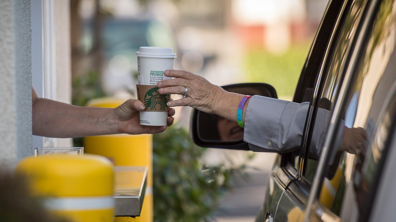 A coffee cup being passed through a Starbucks drive-thru window