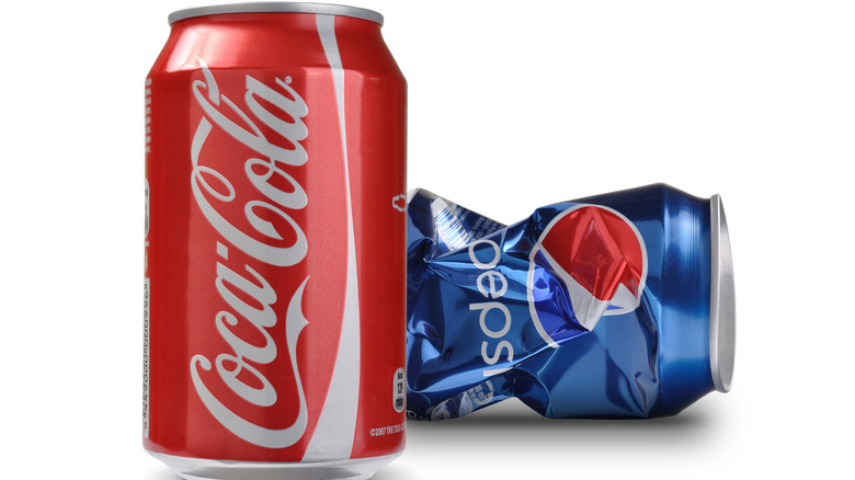 Can of Coke in front of a crumpled Pepsi can 