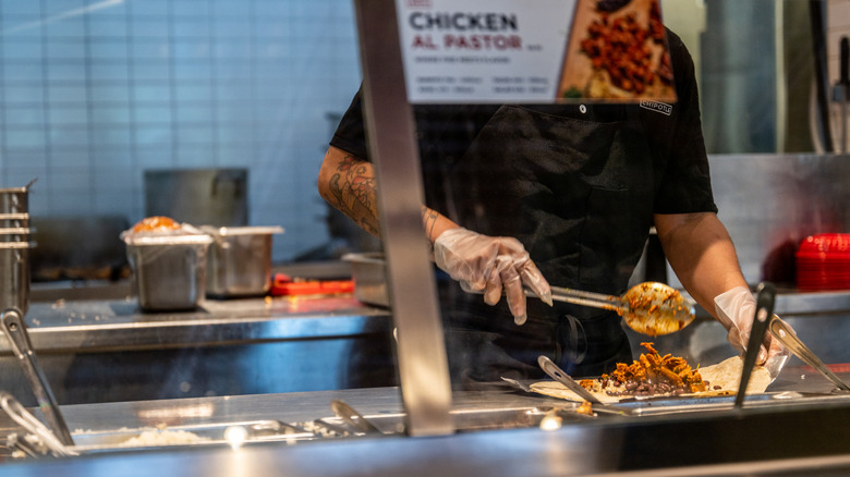 Chipotle employee scooping meat onto burrito.