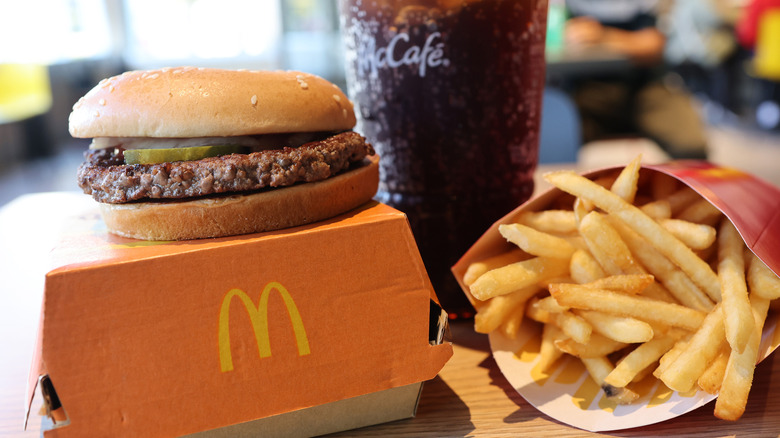 McDonald's quarter pounder on box with fries and cola on wooden-plastic table inside restaurant