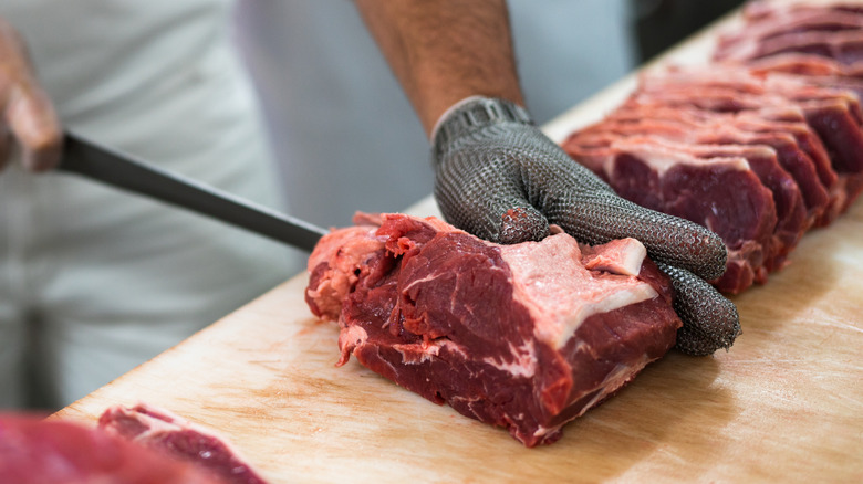 Butcher carving raw steak in a kitchen.