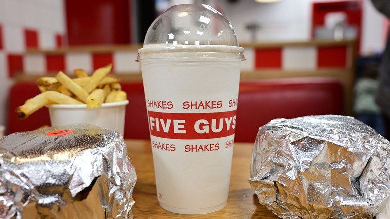 Burgers, fries, and beverage on table at a Five Guys restaurant.