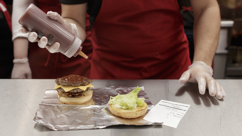 A Five Guys employee squeezes sauce from a bottle onto a burger patty.