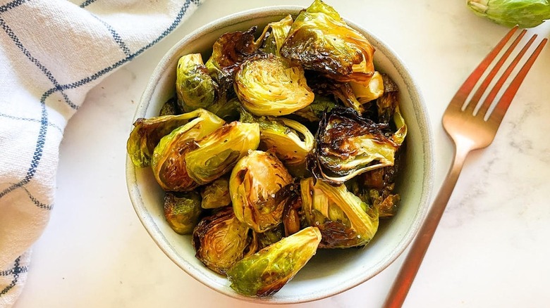 Roasted Brussels sprouts in a bowl next to a fork and a linen napkin