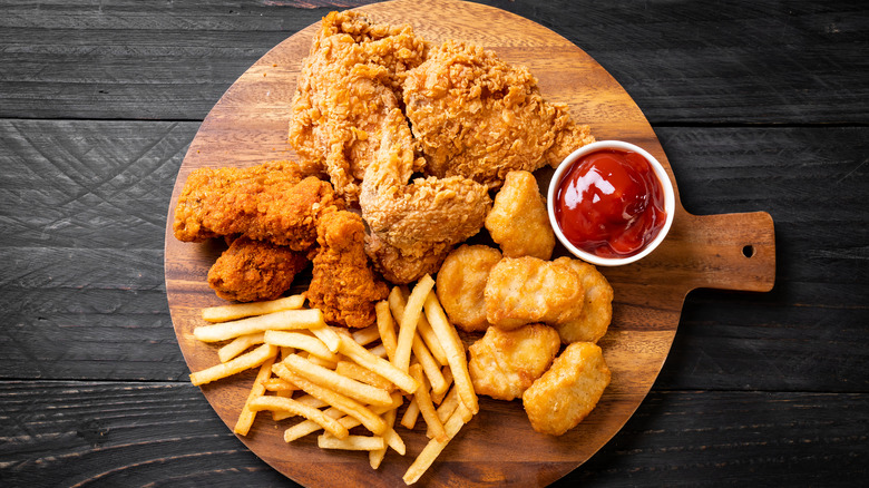 A tray with fried chicken, chicken strips, chicken nuggets, French fries and a container of ketchup.