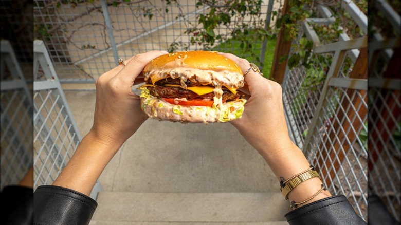 Person sitting outdoors on concrete steps holding an extra large burger from Carl's Jr.