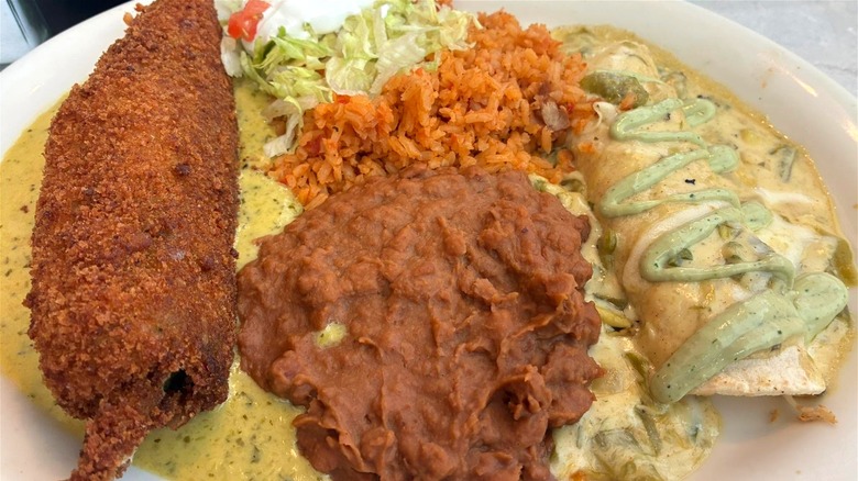 A relleno and enchilada combo platter from Chuy's, served with beans, rice, and veggies.