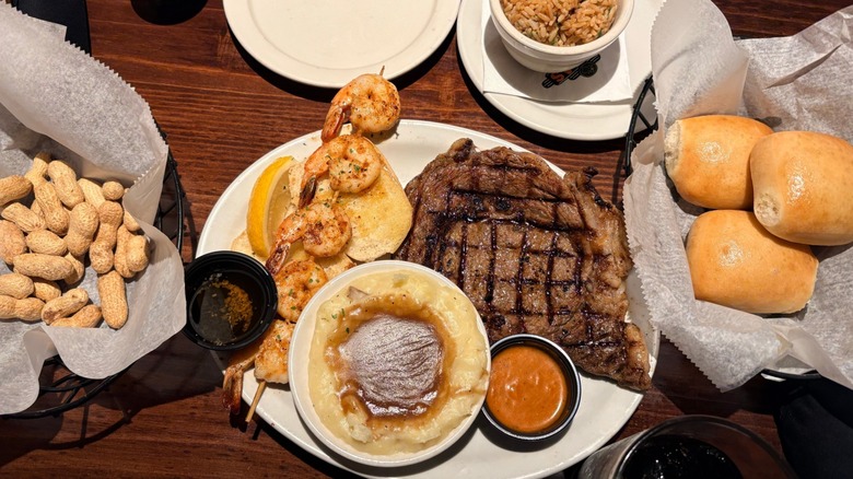 Texas Roadhouse steak, shrimp, rolls, peanuts, and mashed potatoes on table.