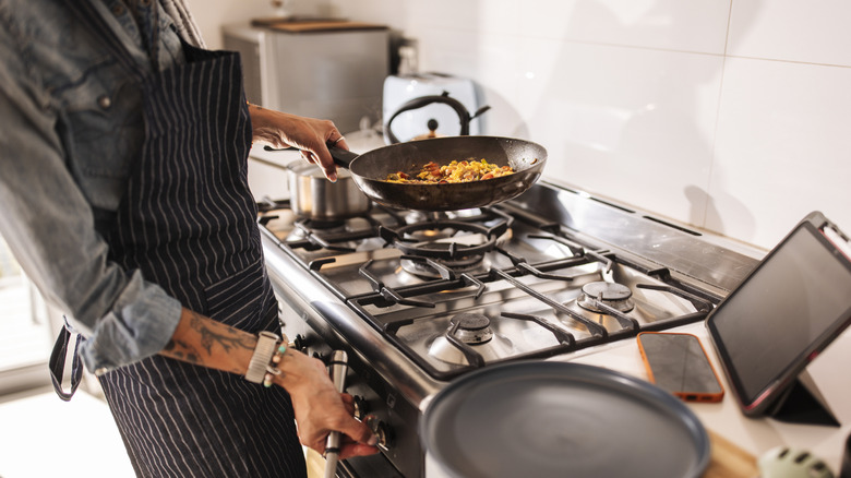 Person holding a pan of food preparing to cook on a gas stovetop.